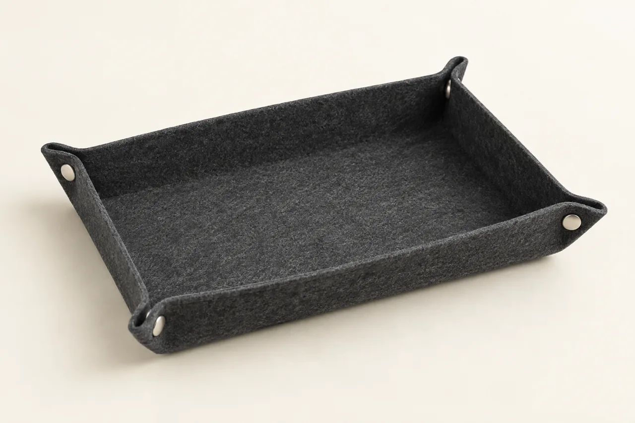 A rectangular charcoal felt tray with low sides and four press-stud corners against an ivory background.